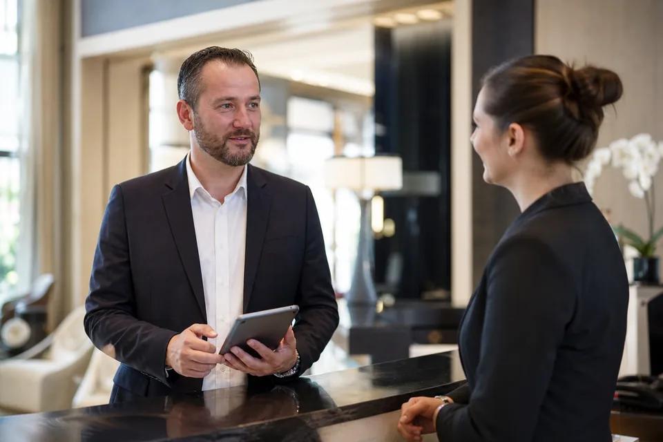 Front desk manager holding a tablet while discussing hiring at a reception desk