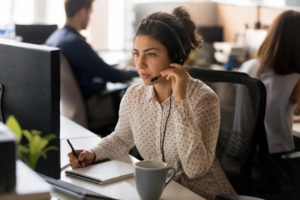 IT staffing recruiter on a headset call at her desk in a busy open-plan office
